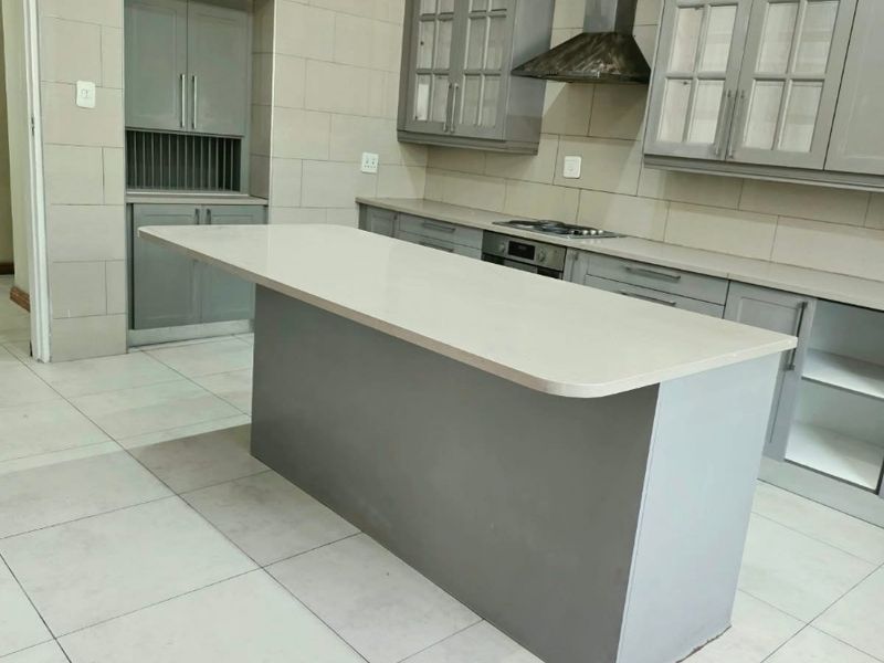 Modern kitchen featuring a central island, grey cabinetry, stone countertops, and integrated appliances, currently awaiting final finishing touches.