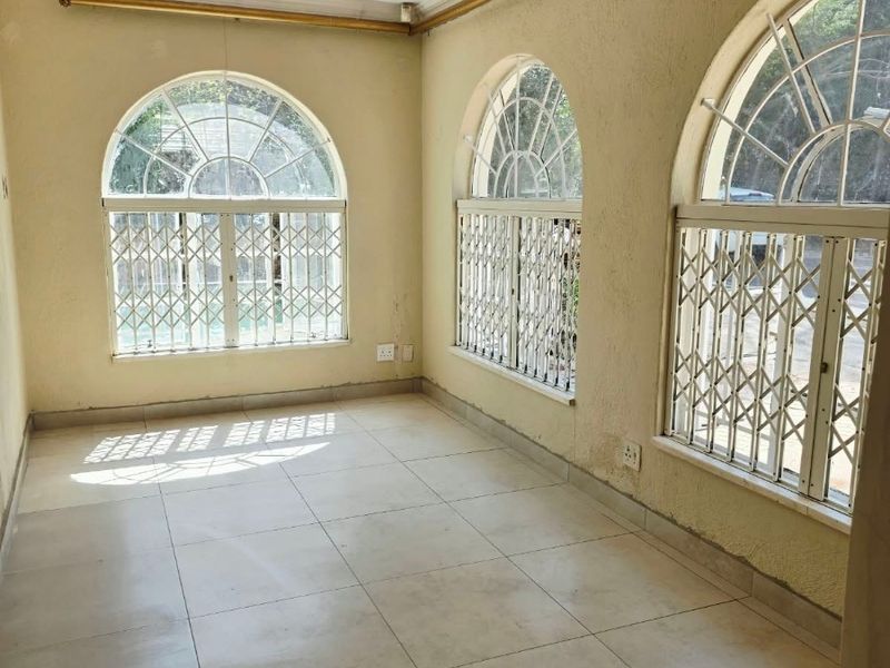 A bright, empty living area featuring arched windows with security bars, tiled flooring, and neutral wall finishes, offering a blank canvas for interior design.