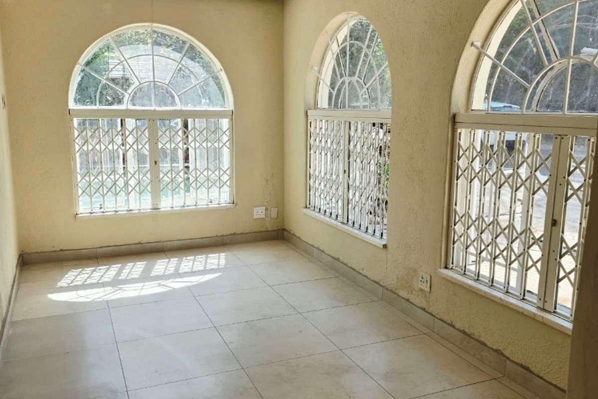 A bright, empty living area featuring arched windows with security bars, tiled flooring, and neutral wall finishes, offering a blank canvas for interior design.