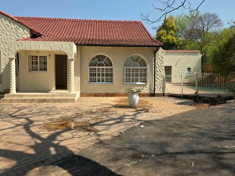 Rear view of a house featuring a textured facade, arched windows, a covered patio, and a swimming pool area with paved surroundings.