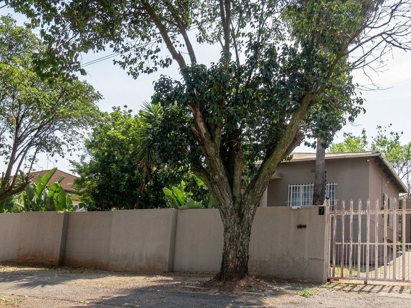 Front view of the property featuring a solid perimeter wall, metal security gate with spikes, and electric fencing, surrounded by mature trees.