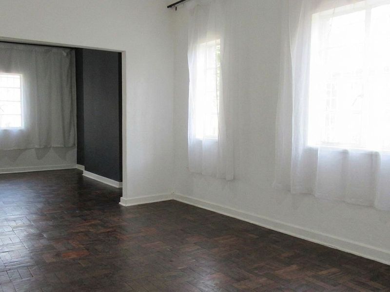 An empty living area featuring dark parquet flooring, white walls, and natural light from multiple windows.