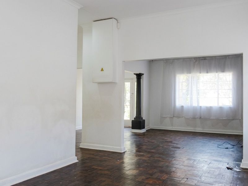 An empty living area featuring dark parquet flooring, a decorative column, and neutral walls, offering a blank canvas for renovation.