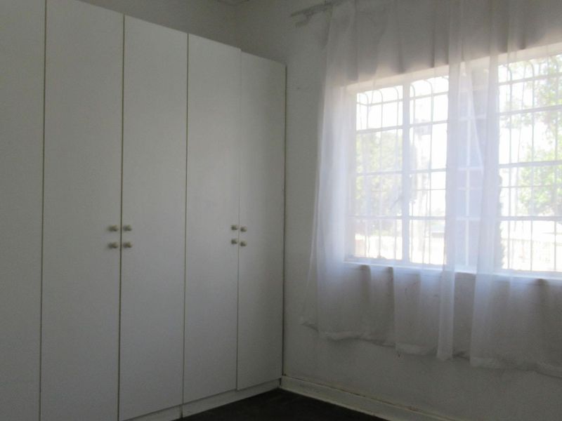 A bedroom featuring built-in cupboards and a window with security bars, offering a functional space ready for personalization.