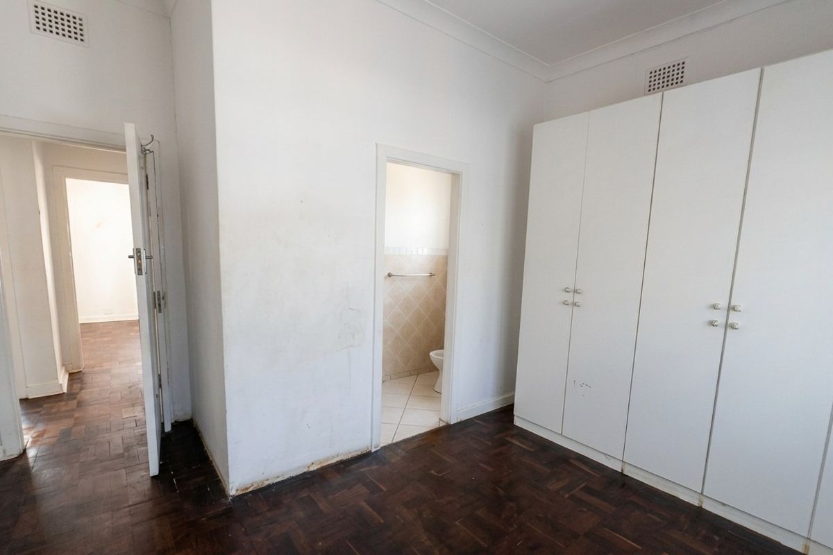 An empty bedroom featuring dark parquet flooring, built-in white cupboards, and an en-suite bathroom access point.