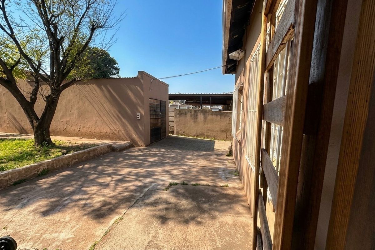 Rear exterior view showing a concrete driveway, perimeter wall, and detached outbuilding with security bars on the windows.