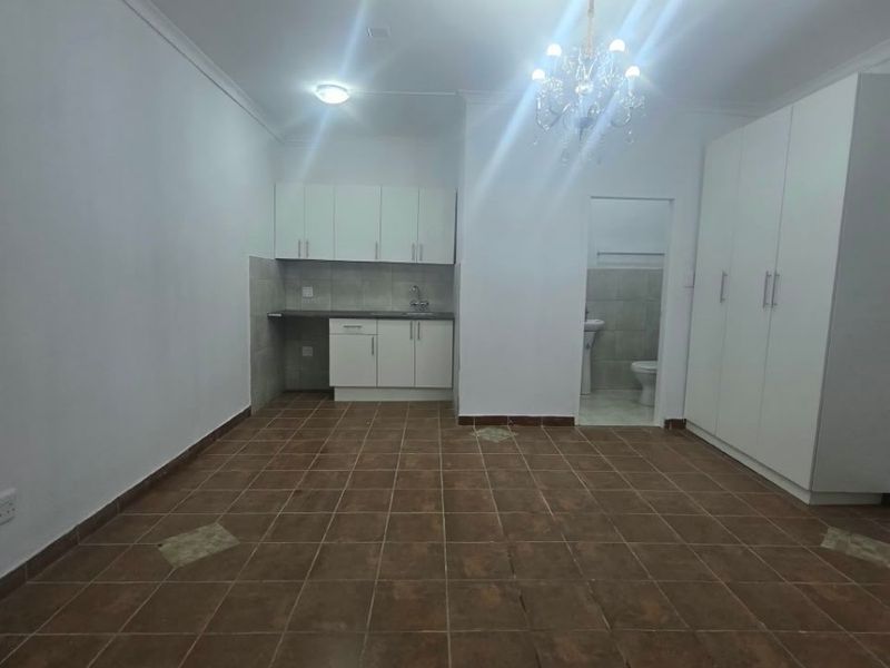 An open-plan living area featuring tiled flooring, built-in kitchen cabinetry, and a built-in wardrobe, with an adjacent bathroom visible.