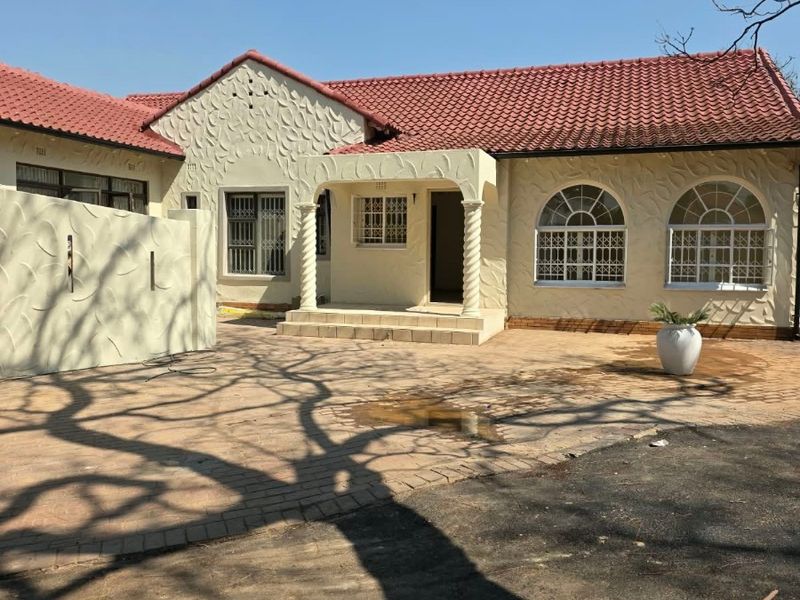 Front elevation of a cottage featuring a tiled roof, textured facade, arched windows with security bars, and a paved driveway with a covered entrance porch.