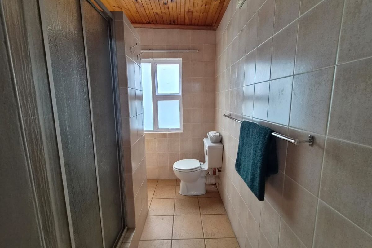 A functional bathroom featuring a shower enclosure, toilet, tiled surfaces, and a timber-paneled ceiling, offering a clean and practical layout.