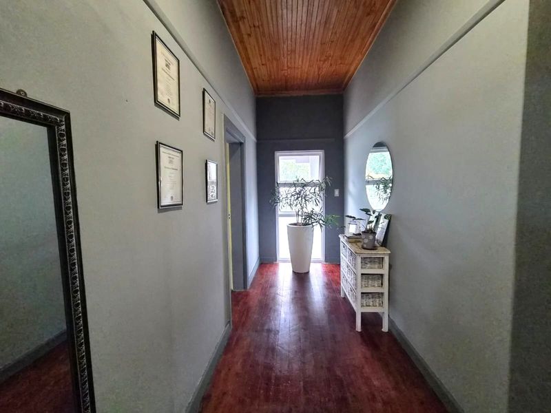 A well-maintained hallway featuring warm timber flooring and a matching timber-paneled ceiling, leading towards a bright window at the end of the passage.