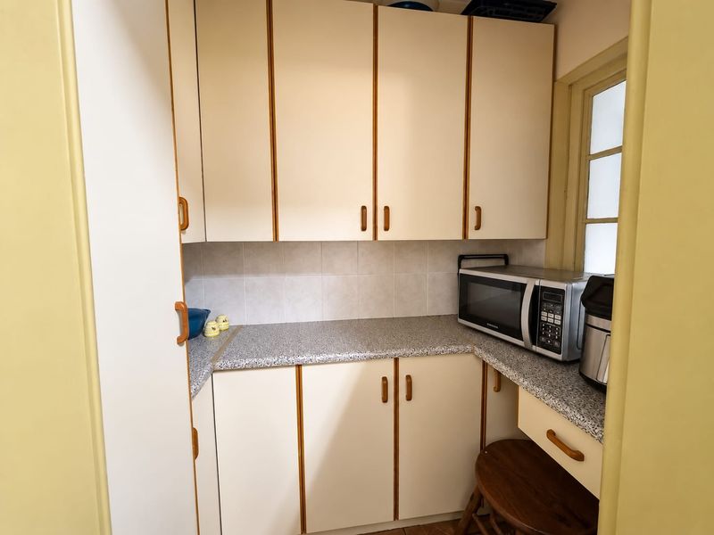 A compact scullery or utility area featuring laminate cabinetry, stone-look laminate countertops, and a tiled backsplash, providing functional storage and prep space.