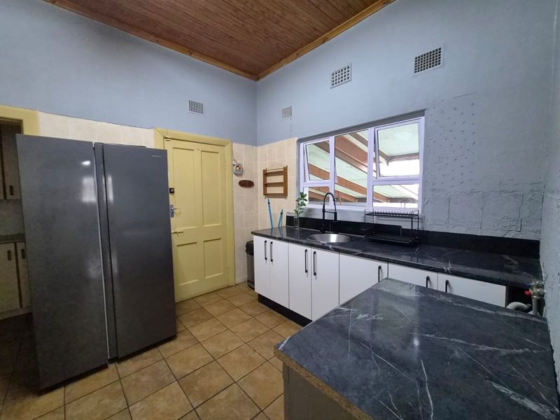 A functional kitchen featuring white cabinetry, dark stone-look countertops, tiled flooring, and a timber ceiling, offering a practical workspace with natural light.