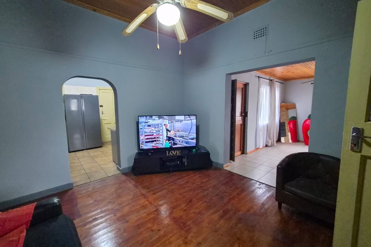 A living room featuring polished hardwood floors, a timber ceiling with a fan, and open access to the kitchen and adjacent living areas.