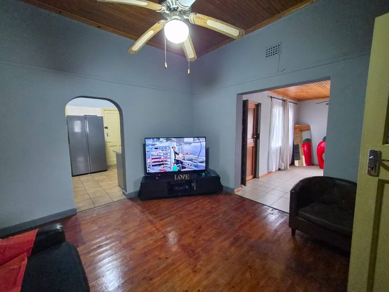 A living room featuring polished hardwood floors, a timber ceiling with a fan, and open access to the kitchen and adjacent living areas.