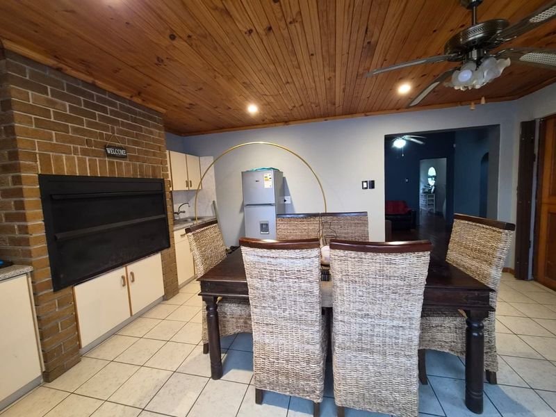 Open plan living and dining area featuring a built-in brick fireplace, timber ceiling, and tiled flooring, offering a functional and rustic layout.