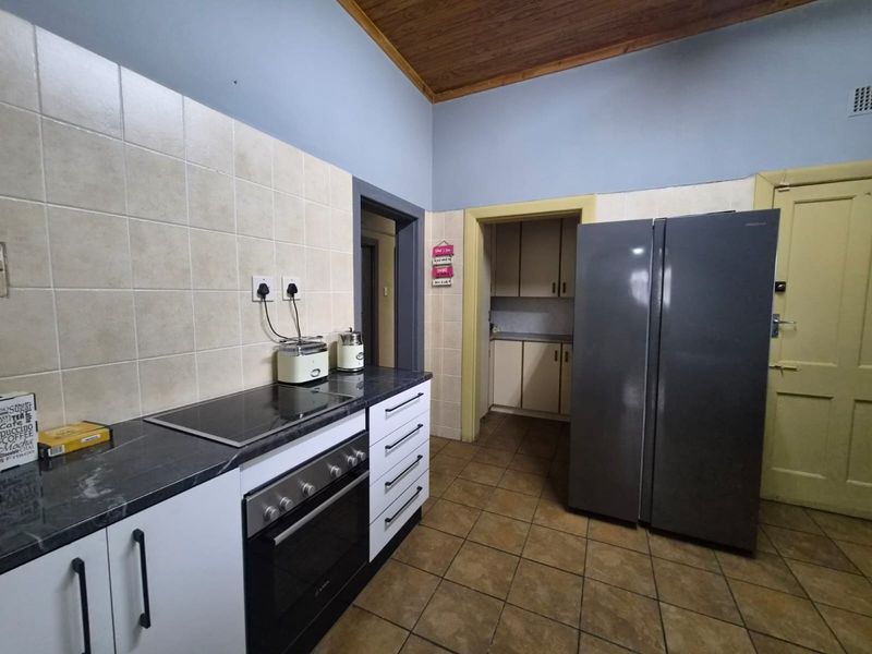 Functional kitchen featuring built-in oven, electric hob, tiled splashback, and ample cabinetry, with a separate scullery area accessible through the doorway.