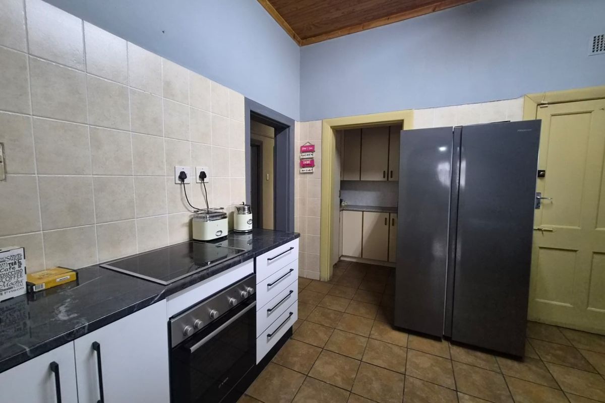 Functional kitchen featuring built-in oven, electric hob, tiled splashback, and ample cabinetry, with a separate scullery area accessible through the doorway.