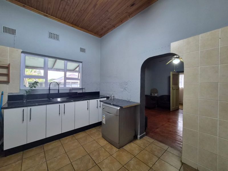 Kitchen featuring white cabinetry, dark countertops, tiled flooring, and a timber ceiling, with an arched doorway leading to the adjacent living area.