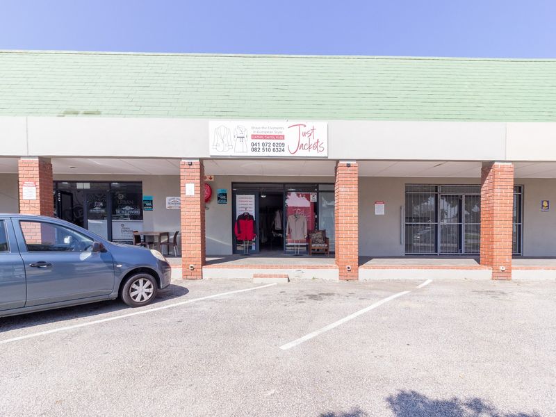 Front exterior view of a retail storefront featuring brick pillars, glass entrance doors, and dedicated parking space in a commercial strip center.