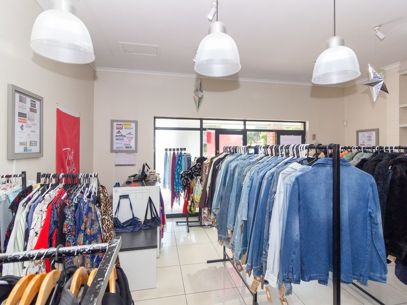 A retail shop interior featuring tiled flooring, pendant lighting, and built-in shelving, currently set up as a clothing boutique.