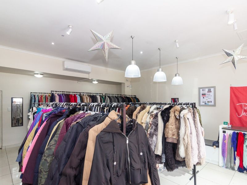 A well-lit retail space featuring tiled flooring, modern pendant lighting, and a wall-mounted air conditioning unit, currently configured as a clothing store.