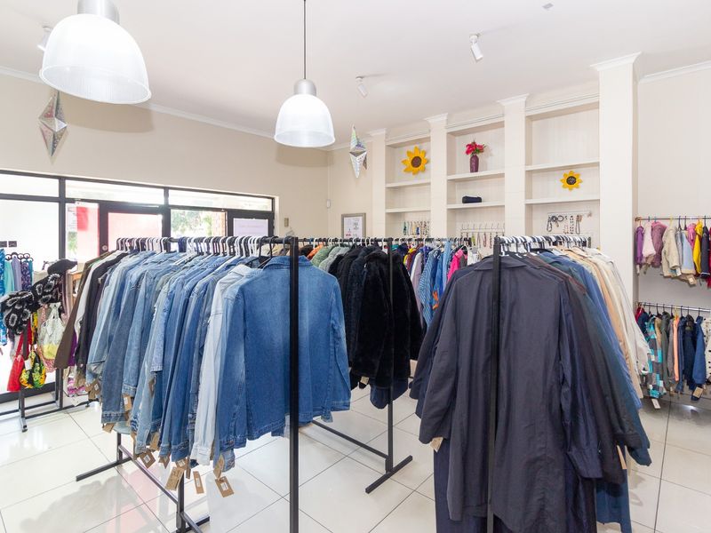 A retail space featuring tiled flooring, built-in display shelving, and modern pendant lighting, currently configured for clothing display.