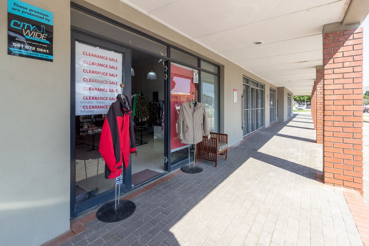 Front exterior view of a retail storefront featuring a paved walkway, brick columns, and glass entrance doors with security gates.