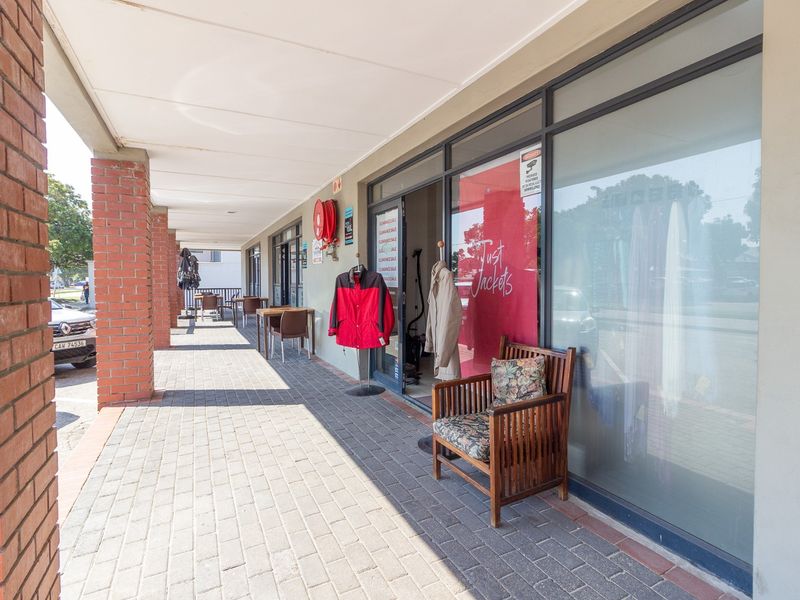 A retail storefront featuring a covered paved walkway, brick support columns, and large glass display windows.