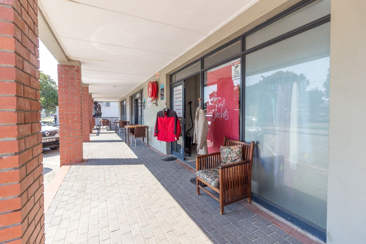 A retail storefront featuring a covered paved walkway, brick support columns, and large glass display windows.