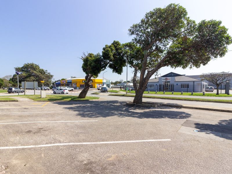 A view of the commercial property exterior featuring an asphalt parking area, mature trees, and surrounding street infrastructure.