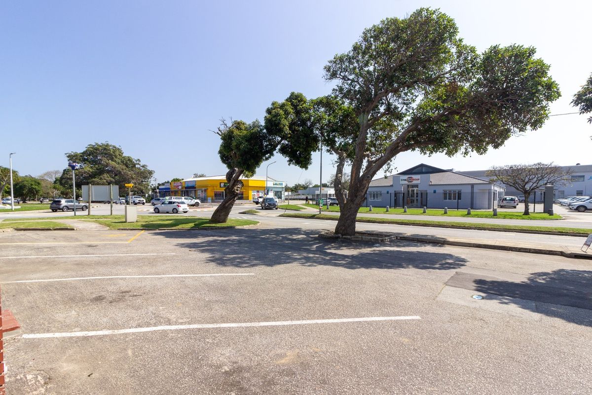 A view of the commercial property exterior featuring an asphalt parking area, mature trees, and surrounding street infrastructure.