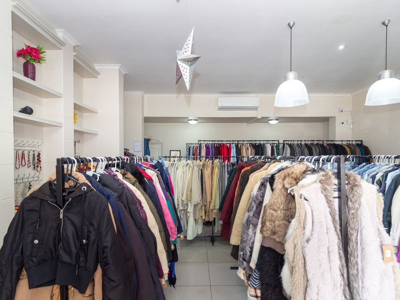 A retail clothing store interior featuring built-in shelving, tiled flooring, and modern pendant lighting, currently set up with clothing racks.