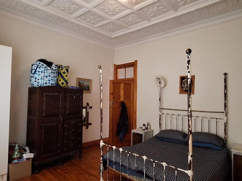 A bedroom featuring a classic pressed metal ceiling, original timber flooring, and a traditional timber door, offering a character-filled space with potential for updates.