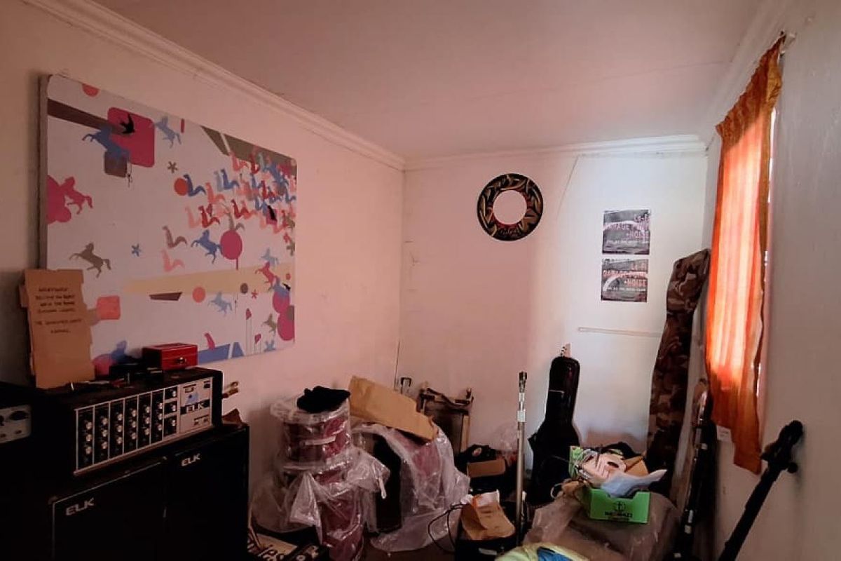 A small bedroom space with plain white walls and a single window, currently used for storage.