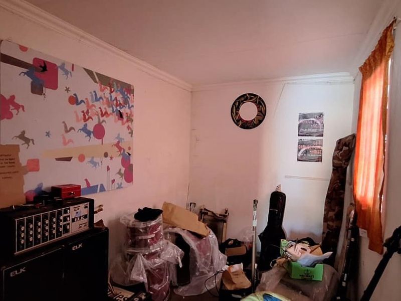 A small bedroom space with plain white walls and a single window, currently used for storage.
