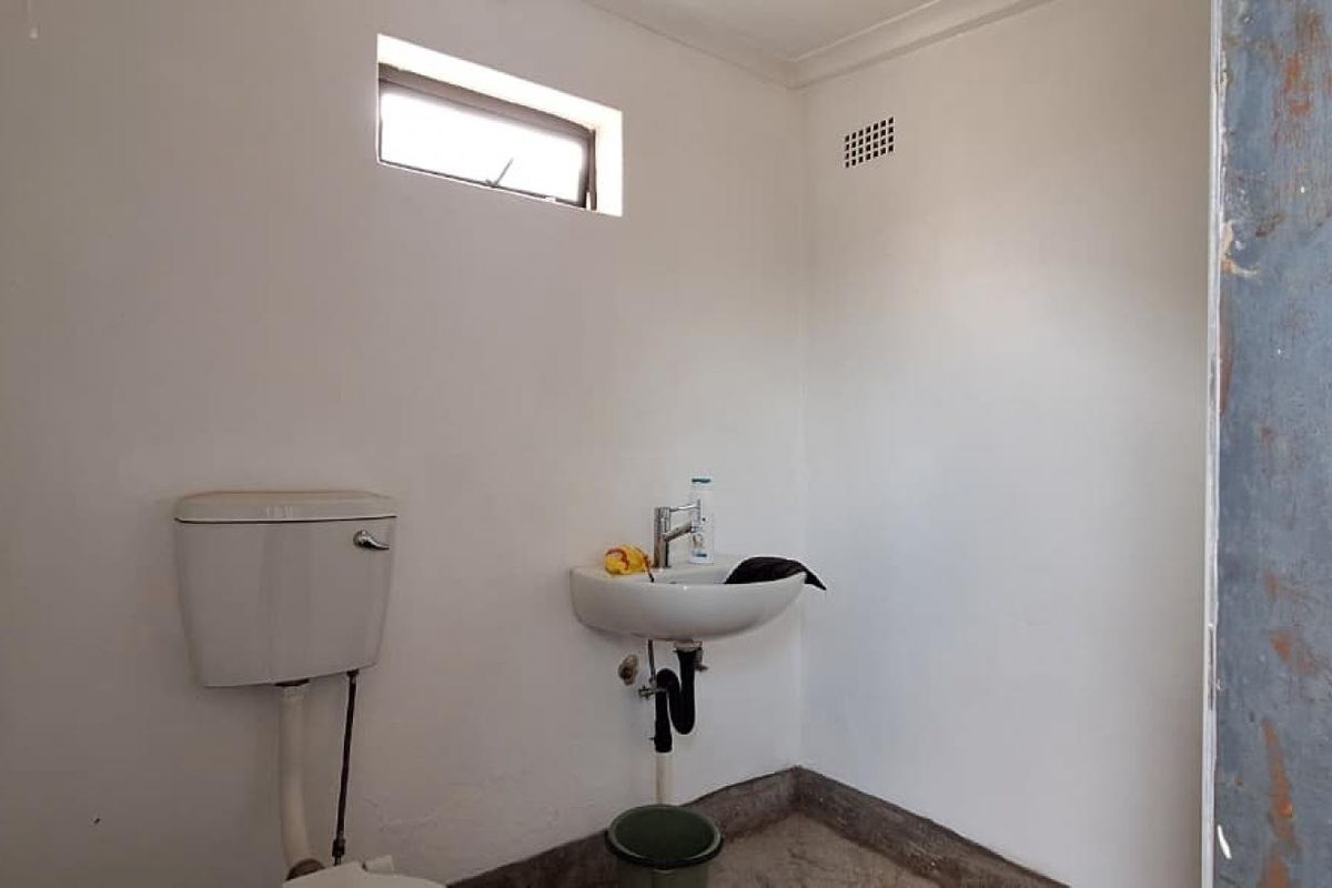 A basic, functional bathroom featuring a wall-mounted basin and toilet, requiring cosmetic updates to the door frame and finishes.