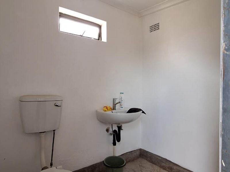 A basic, functional bathroom featuring a wall-mounted basin and toilet, requiring cosmetic updates to the door frame and finishes.