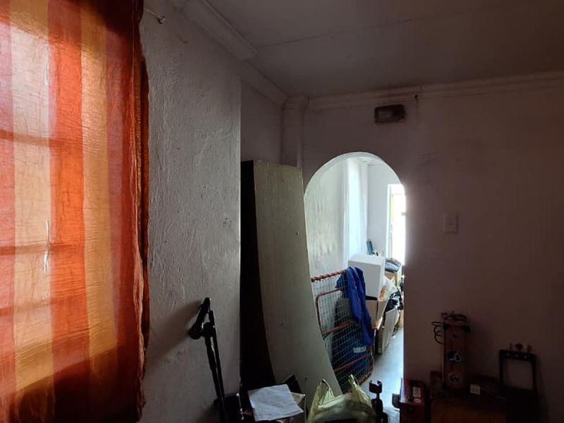 A living area featuring an arched doorway and coved cornicing, currently requiring significant cosmetic refurbishment and wall repairs.