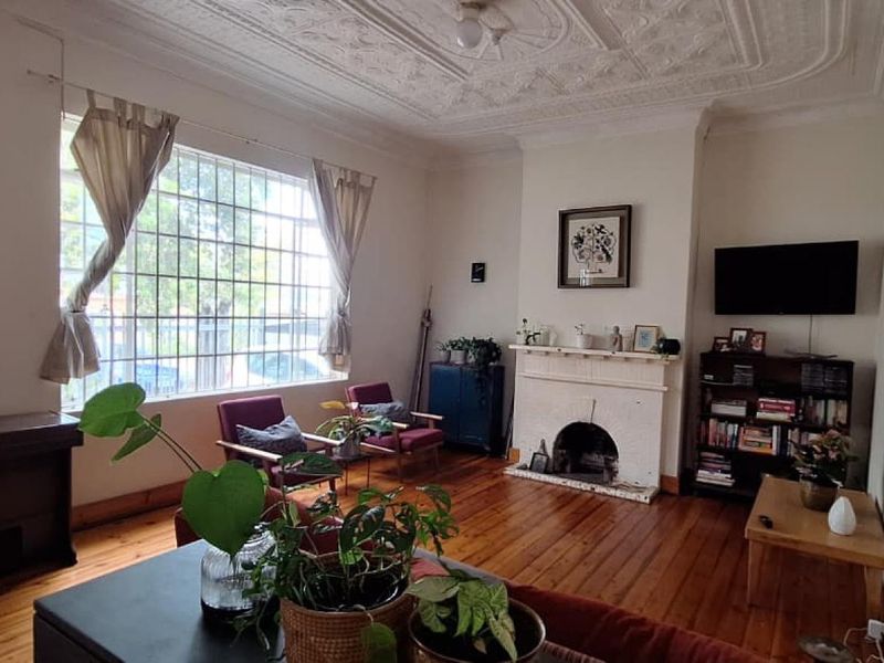 Spacious living room featuring original hardwood flooring, an ornate plaster ceiling, and a classic fireplace, offering a character-filled space with large windows.