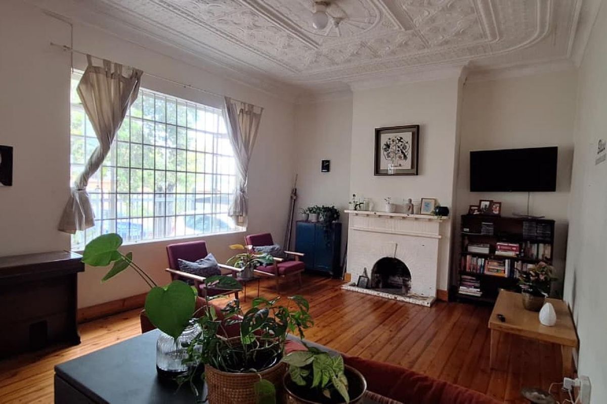 Spacious living room featuring original hardwood flooring, an ornate plaster ceiling, and a classic fireplace, offering a character-filled space with large windows.