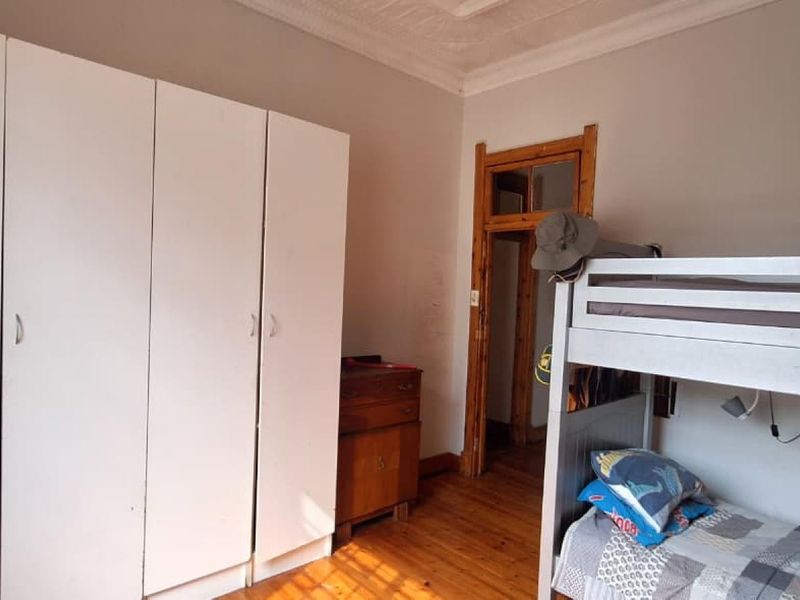 A bedroom featuring timber flooring, ornate ceiling detailing, and a built-in wardrobe, offering a functional space with classic architectural character.