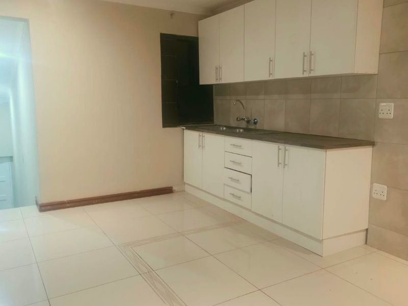 A clean, modern kitchen featuring white built-in cabinetry, a neutral tiled backsplash, and light-colored floor tiles in an open-plan layout.