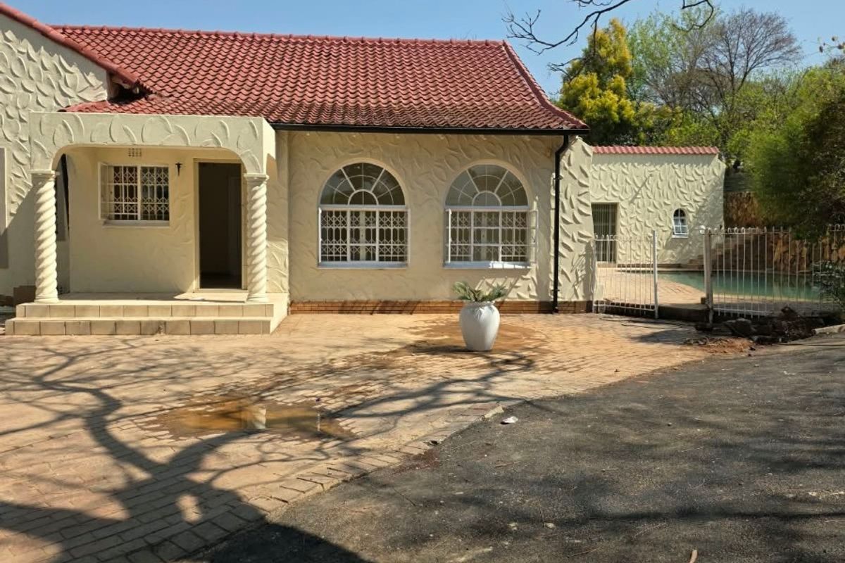 Rear view of a house featuring a textured facade, arched windows, a covered patio, and a swimming pool area with paved surroundings.