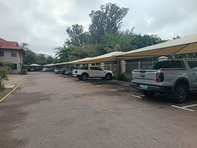 Exterior view of an office property featuring a paved parking area with multiple shade cloth carports and perimeter fencing.