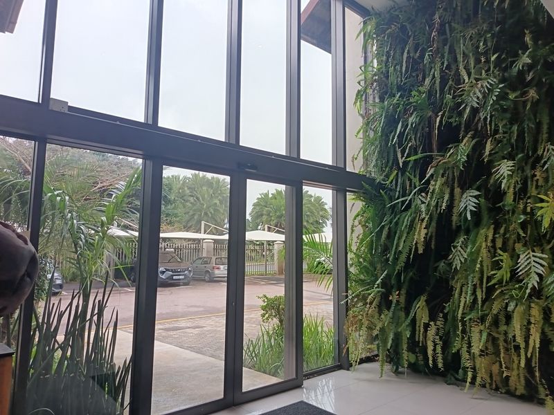 Modern office entrance featuring a striking vertical garden wall, expansive floor-to-ceiling glass facade, and automatic sliding doors with views of the parking area.