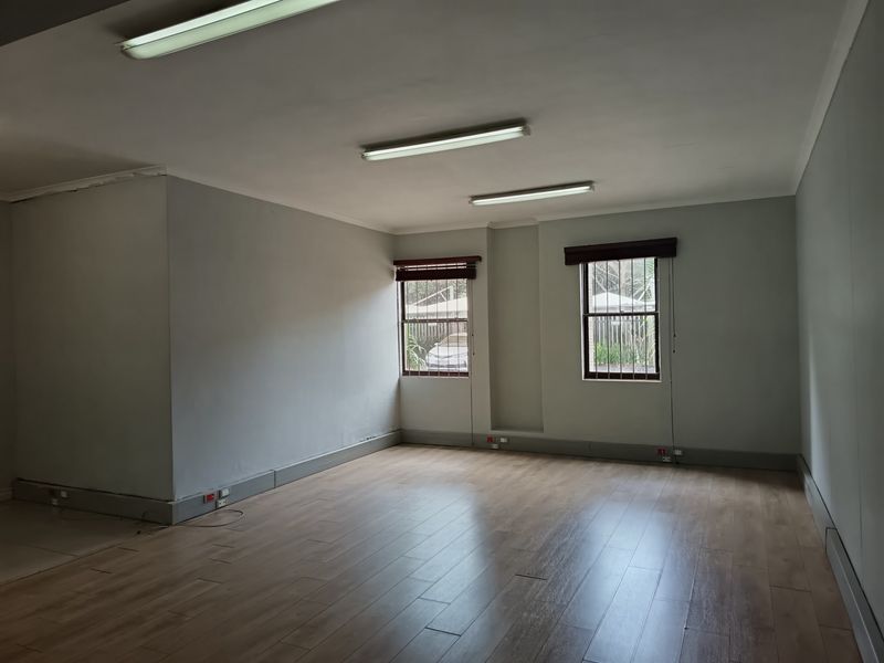 A vacant office space featuring laminate flooring, fluorescent lighting, and security bars on the windows, providing a clean and functional workspace.