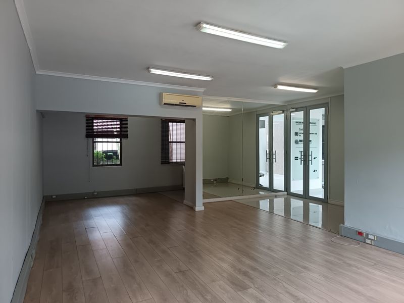 A spacious, vacant office suite featuring laminate flooring, mirrored wall accents, glass-paneled entry doors, and integrated air conditioning.