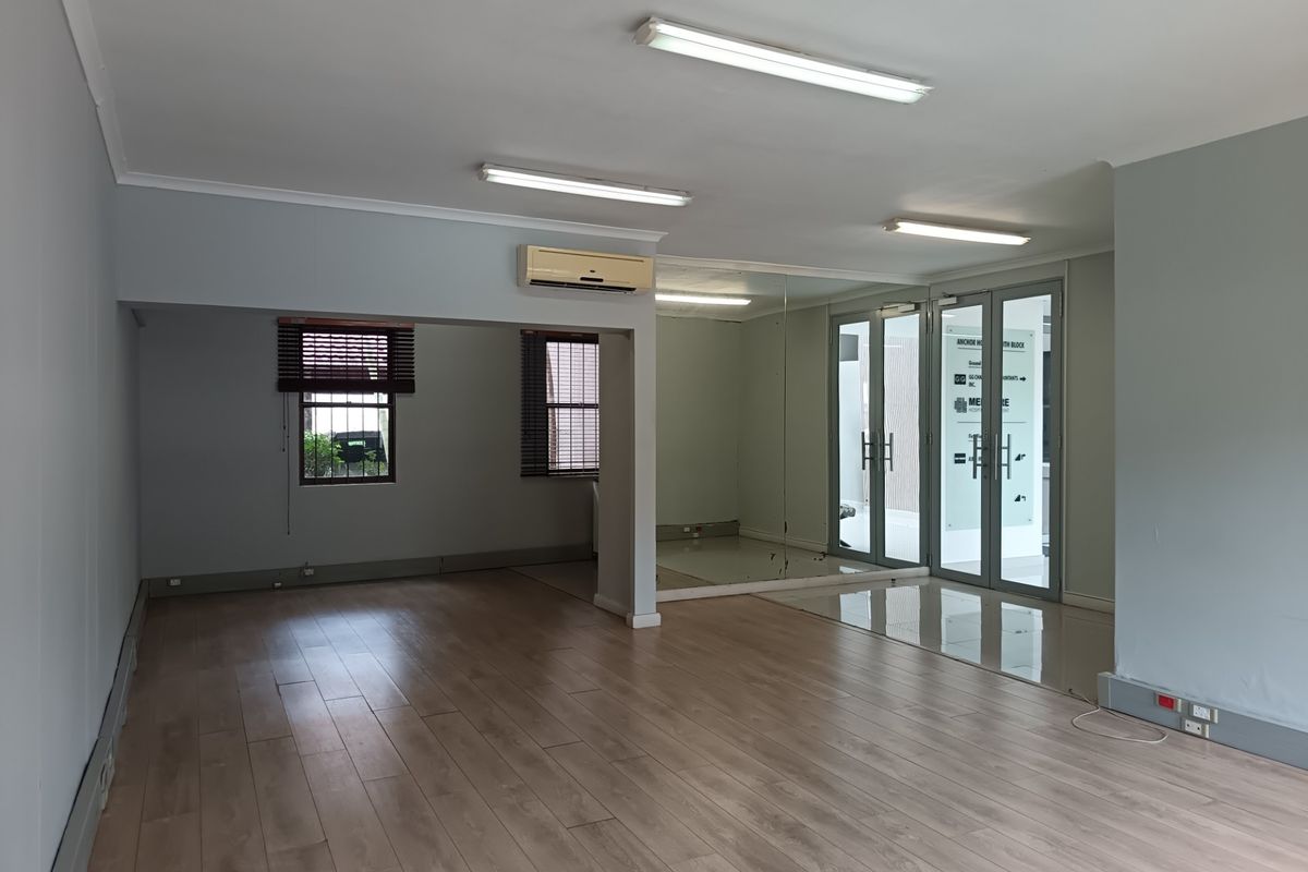 A spacious, vacant office suite featuring laminate flooring, mirrored wall accents, glass-paneled entry doors, and integrated air conditioning.