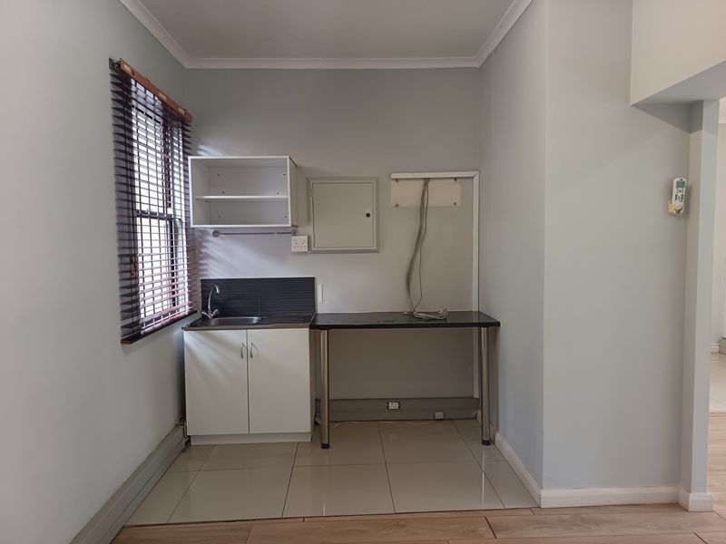 A compact kitchenette area featuring a stainless steel sink, built-in cabinetry, tiled splashback, and tiled flooring, suitable for an office breakroom or utility space.