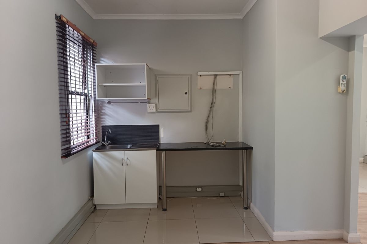 A compact kitchenette area featuring a stainless steel sink, built-in cabinetry, tiled splashback, and tiled flooring, suitable for an office breakroom or utility space.
